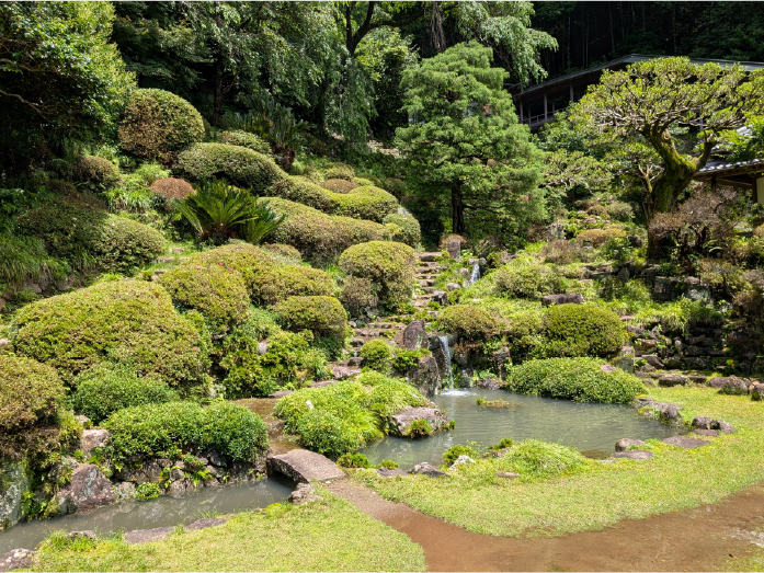 池と小さな滝、石段が配された緑豊かな日本庭園の風景